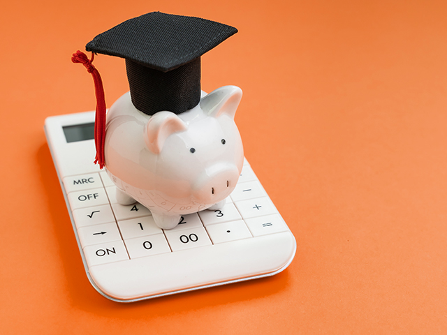 piggy bank in graduation cap sitting on a calculator